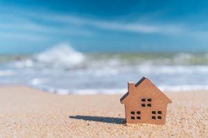 Small,Home,Model,On,Sand,Beach,With,Blue,Sky,And